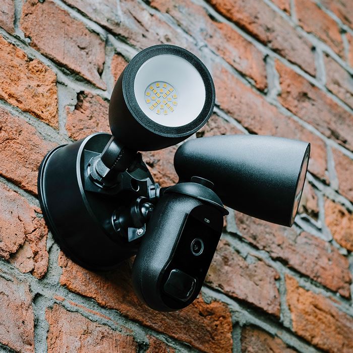 Close up of a black Amalock CAM-600FL-AC floodlight security camera  mounted on a red brick wall