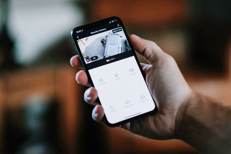 A hand holding a smartphone showing a livestream HD video from an Amalock floodlight security camera
