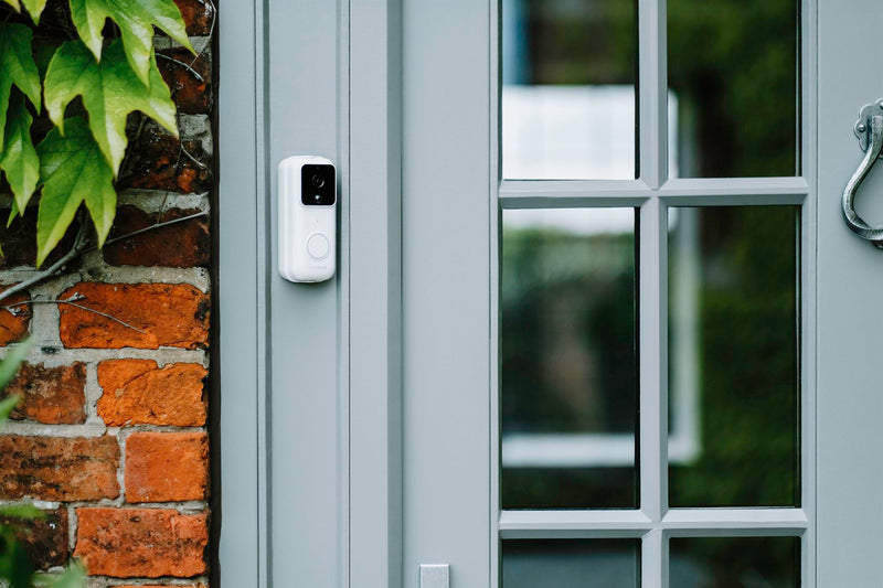 A white Amalock DB301 wireless video doorbell mounted on an angle bracket on a grey doorframe.