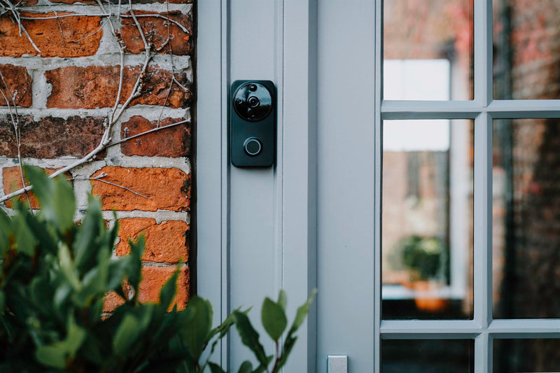A black Amalock DB101 wireless video doorbell facing forward mounted on a grey doorframe