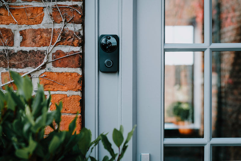 A black Amalock DB101 wireless video doorbell mounted on a grey doorframe