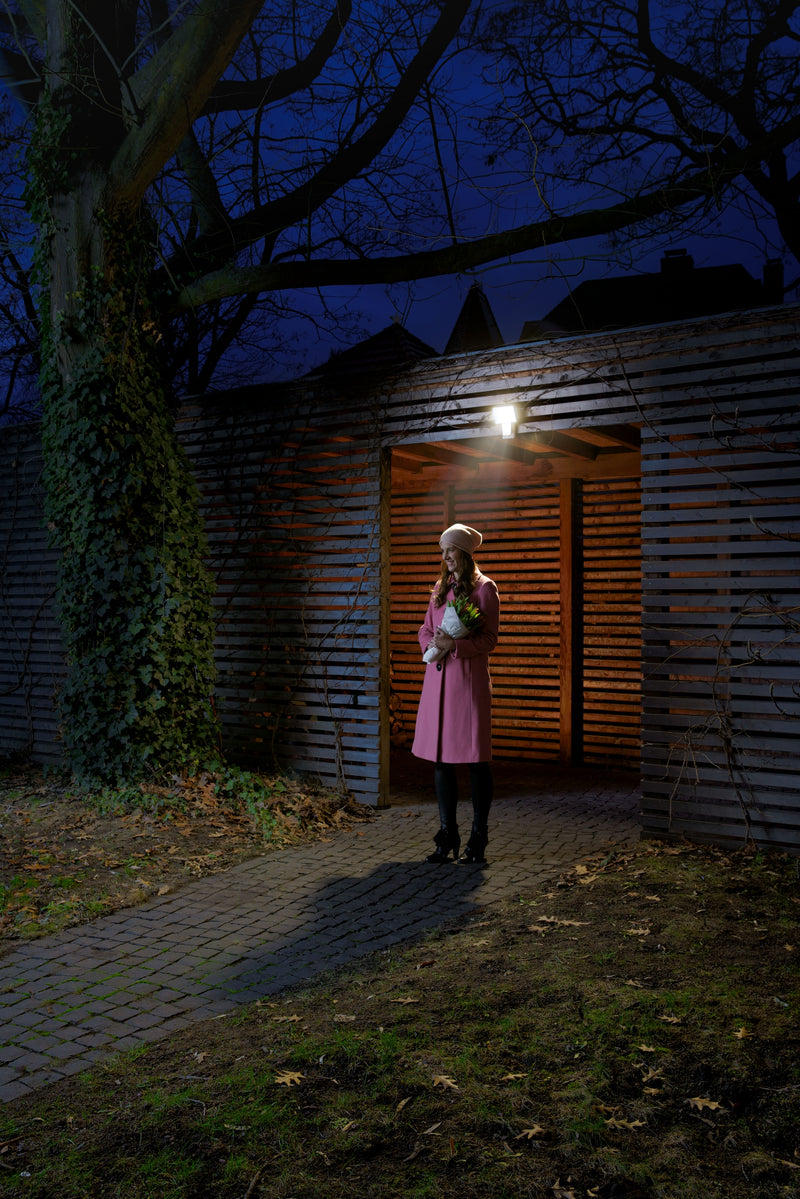 A Ledvance Endura Pro Flood Sensor 27W cool white LED outdoor floodlight with integrated motion sensor and adjustable lamp head mounted on an outbuilding wall, illuminated at night. 