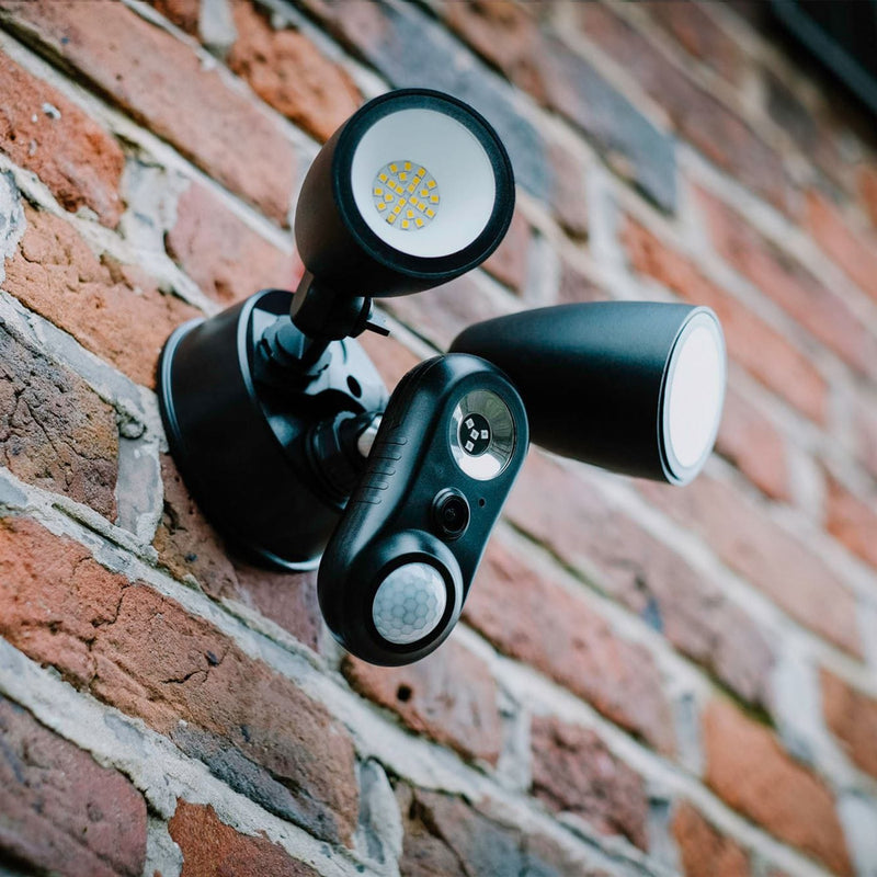 Close up of a black CAM-600FL plug-in floodlight security camera mounted on a red brick wall