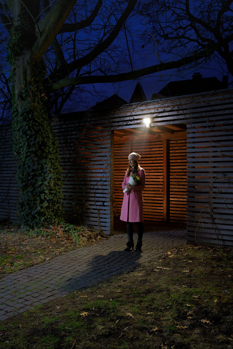 A Ledvance Endura Pro Flood Sensor 27W cool white LED outdoor floodlight with integrated motion sensor and adjustable lamp head mounted on an outbuilding wall, illuminated at night. 