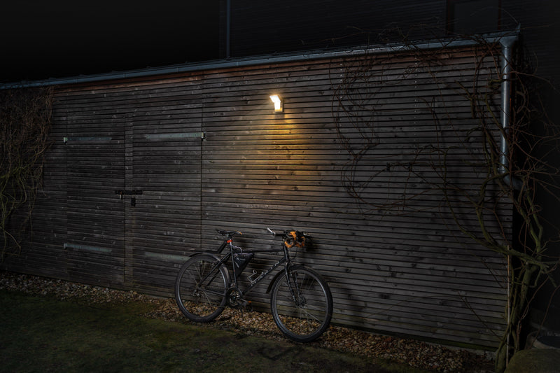 Ledvance Endura Pro Spot Sensor 16W cool white LED outdoor twin spotlight positioned on a garage wall with a bike leaning up against it with spotlights on at night 